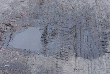 one big puddle with dirty water on the gray ground of the road outside