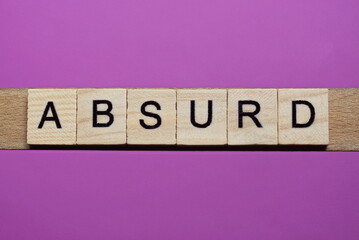 word absurd from small gray wooden letters lies on a purple background