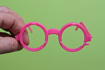 Fototapeta premium fingers on the hand hold one plastic pink toy glasses on a green background