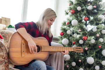 young woman holds a guitar in hand and sits in christmas studio