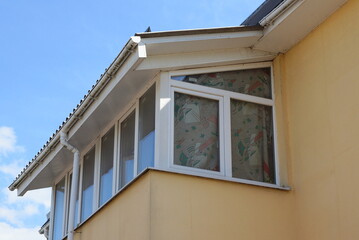 one white closed glass balcony in the brown attic of a private house against the sky