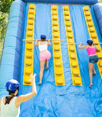 Two active sporty young women having funny competition in climbing on inflatable castle with wooden...