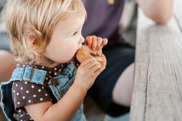 A cute toddler girl holding and eating a cinnamon sugar donut