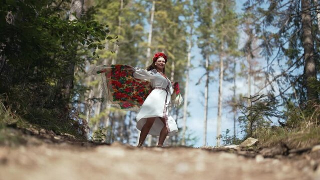 Beautiful ukrainian woman dancing with handkerchief in fir forest, Carpathian mountains nature. Girl in traditional embroidery vyshyvanka dress. Ukraine, freedom, ethnic national costume