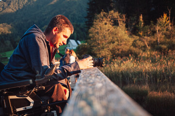 Young photographer with disability taking a photo of mountain nature at dusk, enjoying stunning...