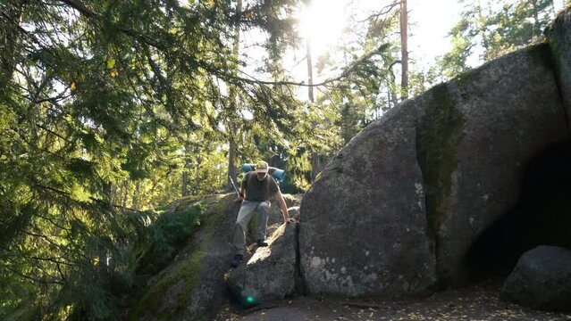 A mature male adventurer with hiking equipment exploring a forest cave alone. Hogberget Cave in South Finland.