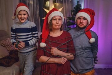 The son entangles and binds the parents at the Christmas tree in the night light of the garland....