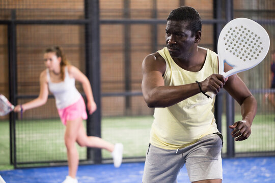 African male player ready to hits the ball while playing padel on a hard court