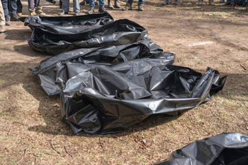 Several empty corpse body bag lie on the ground. People gathered around.