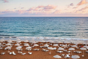 Sun loungers on the sandy beach, sea and clouds at sunset