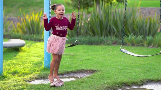 ni&ntilde;a sin dientes festejando celebrando en parque brincando en charco con agua de lluvia y lodo con tierra sucia disfrutando y divertida en el parque al exterior al aire libre en un hermoso d&iacute;a