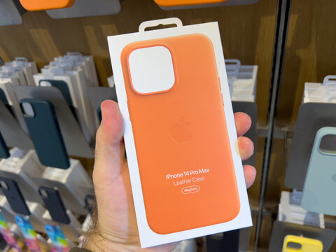 Paris, France - Sep 16, 2022: POV male hand holding package in Apple Store shopping with new orange iPhone 14 Pro Max leather case with MagSafe charging