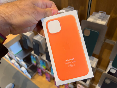Paris, France - Sep 16, 2022: POV male hand holding package in Apple Store shopping with new orange iPhone 14 leather case with MagSafe charging