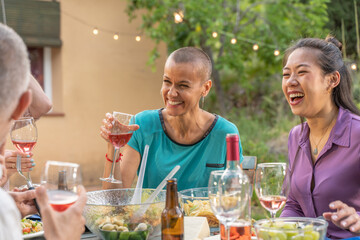Multiracial friends eating and drinking happy smiling and laughing in the patio. Middle-aged cheerful people around the table.