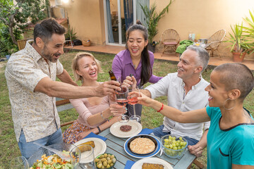 Multiracial friends toasting and enjoying with wine around the table at house patio diner.