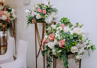 Obraz na płótnie Canvas Beautiful multi-colored flowers stand on a bronze rack against a background of a white wall in a restaurant, interior. Wedding decorations, photography.