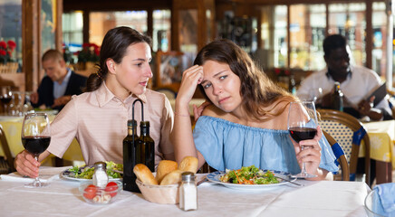 Depressed young girl complaining to her friend about her husband in a restaurant