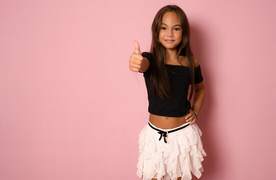 Little smiling girl showing thumbs up on a pink background.