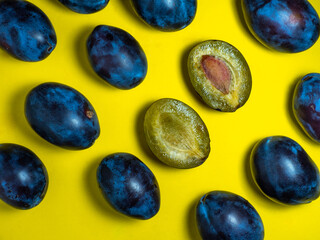 Plums on a yellow background. Juicy sliced ​​plum. Stone in yellow pulp. Healthy food concept. Sweet purple variety. Fruit pattern.