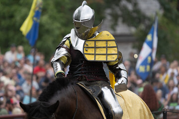 unknown knight in a suit of armor is riding on a horse and ready for battle