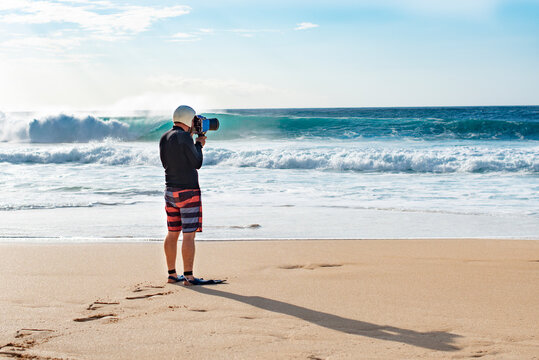 A surf photographer taking photographs by the shore at Banzai Pipeline, Oahu, Hawaii, USA