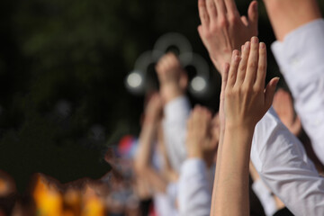 A group of young people with their hands up and clapping in a gesture of approval at a concert