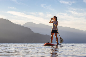 Adventurous Woman Paddling on a Paddle Board in a peaceful lake.