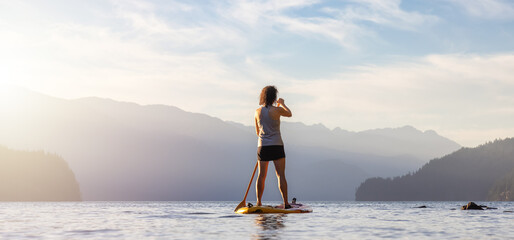 Adventurous Woman Paddling on a Paddle Board in a peaceful lake.