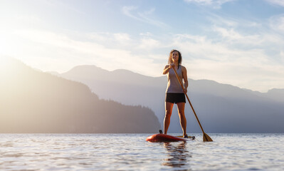 Adventurous Woman Paddling on a Paddle Board in a peaceful lake.