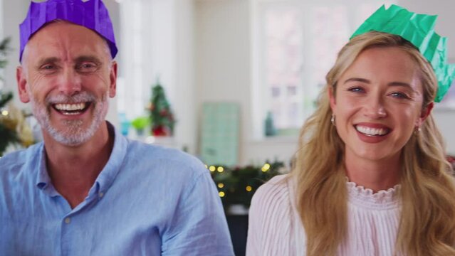 Camera tracks across faces of multi-generation family celebrating Christmas at home wearing hats from party crackers before eating meal together - shot in slow motion