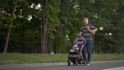 A man rolls a baby around the park and eats a burger. Young father with his son for a walk.