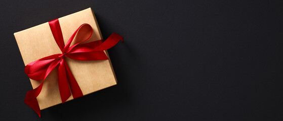 Craft paper gift box with red ribbon bow on black background. Black Friday banner template.
