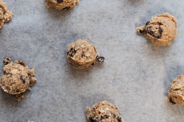 Close up of round raw oatmeal raisin cookie dough scoops on cookie sheet with baking paper made of flour, rolled oats, sugar, eggs, raisins, dried fruit, baking soda and powder before baking - 531552633