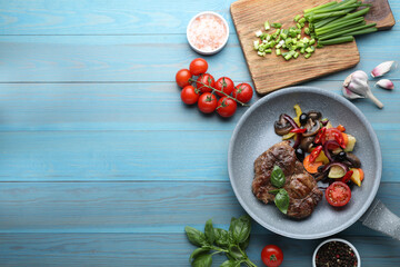 Tasty fried steak with vegetables in pan and ingredients on light blue wooden table, flat lay. Space for text