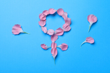 Female gender sign made of petals on light blue background, top view. Women's health concept