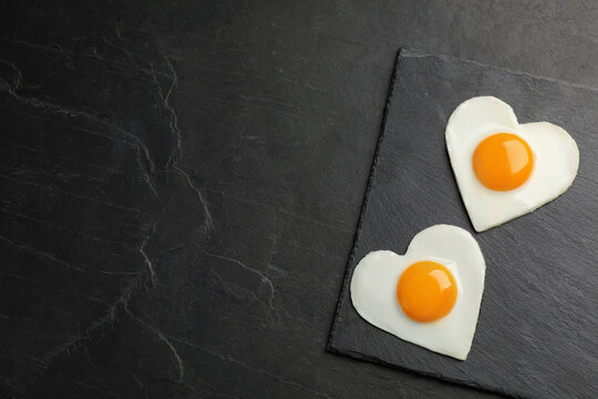 Heart shaped fried eggs on black table, top view. Space for text