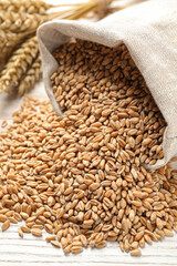 Sack with wheat grains on white wooden table, closeup