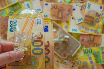 Electricity cost in Europe.Electric light bulb in hand on euro bills background. Rising electricity prices.Energy production crisis in European countries.