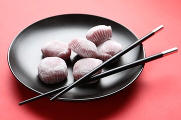 Black plate with delicious mochi and chopsticks on red background. Traditional Japanese dessert