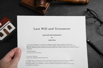 Woman holding last will and testament at black table, top view