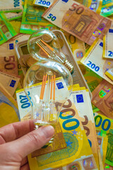 Electric light bulb in hand on euro bills background. Rising electricity prices.Paying electricity...