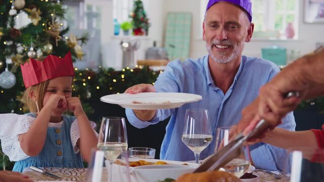 Multi-generation family celebrating Christmas at home wearing hats from party crackers with father carving turkey for meal together - shot in slow motion
