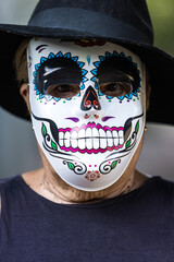 Portrait of an elderly lady with a catrina mask and hat, celebrating Halloween and All Souls' Day, on the street. Celebration, costume, party and mask concept.