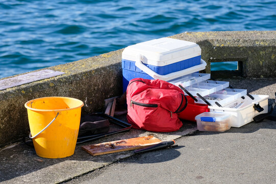 Colourful red, yellow and blue fishing tackle, gear,  equipment, and cool box, on the pier with water, ocean, sea in background