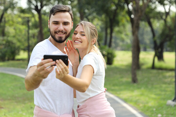 young caucasian couple in love using smart mobile phone portrait themself in the park (relaxation with technology concept)