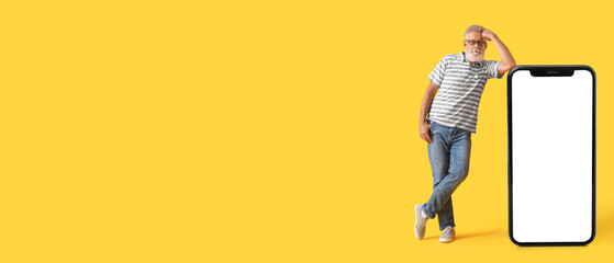 Mature man and big smartphone on yellow background with space for text