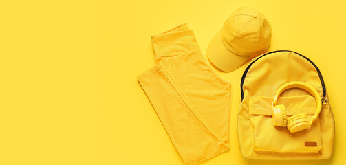 Sportswear, cap, backpack and headphones on yellow background with space for text