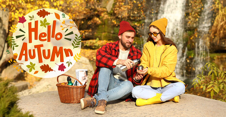 Fototapeta na wymiar Couple in warm clothes having picnic near waterfall on sunny day. Hello autumn