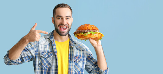 Young man holding tasty burger on light blue background with space for text