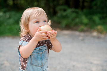Cute little one-year old girl eats an apple outside in overalls
